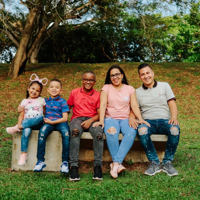 A Hispanic family with three children sitting together on a park bench, the kind of household Rapido Refunds files for