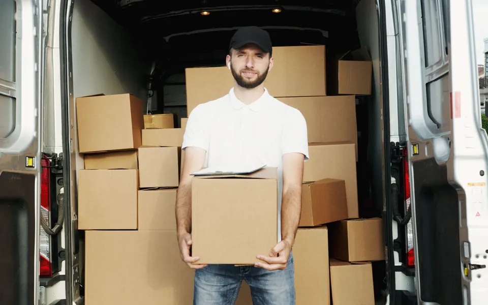 A delivery driver holding a package beside his van